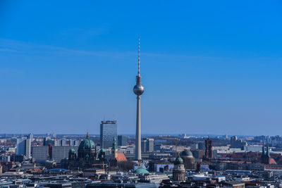 Communications tower in city against blue sky