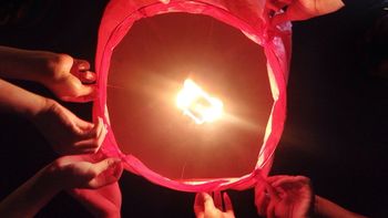 Cropped hands of friends holding illuminated paper lantern at night