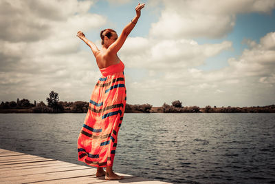 Full length of young woman standing by lake against sky