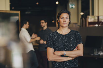 Portrait of businesswoman standing arms crossed with colleagues in background at office