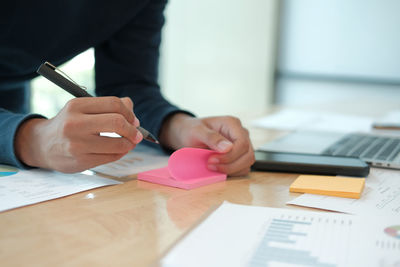 Midsection of businessman writing on adhesive note at table in office 