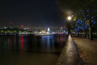 Illuminated city by river against sky at night