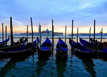 Gondola boats moored in water against st mark cathedral during sunset