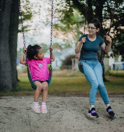 Cute girl sitting on swing with mother at playground