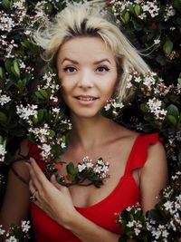 Portrait of smiling young woman standing by flowering plants