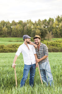 Portrait of happy male farm worker with coworker standing on agricultural field against sky during sunset