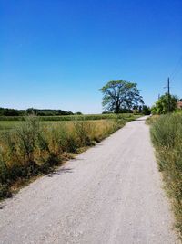 Road amidst field against clear blue sky