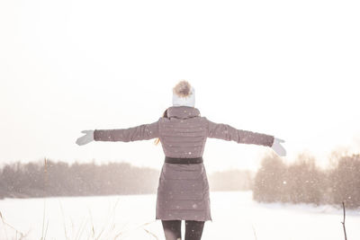 Rear view of woman standing on snow covered landscape against sky