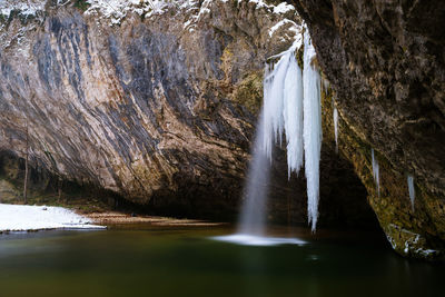 Low angle view of water flowing from rock formation during winter