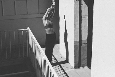 Young woman stretching arm while standing by railing