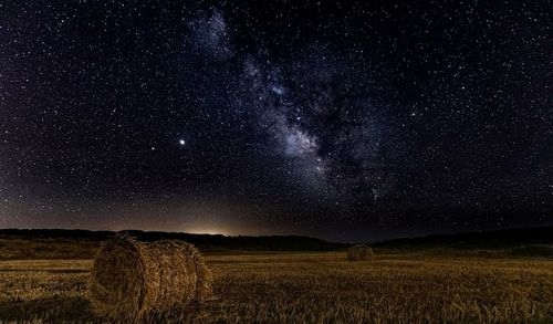 Hay bales on field against sky at night