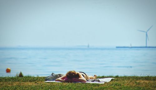 Woman lying on grass at beach against sky