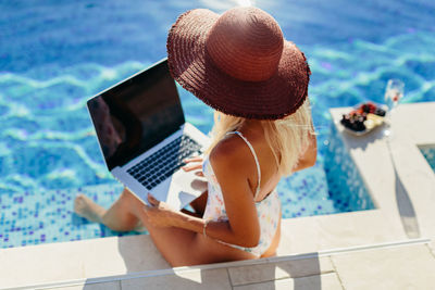 Rear view of woman using mobile phone in swimming pool