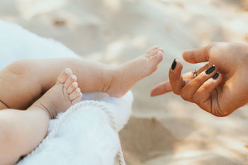 Cropped hand of mother with baby lying on bed