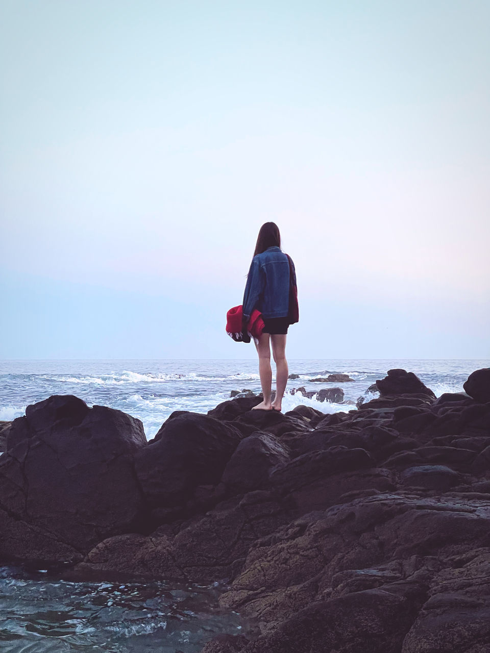 REAR VIEW OF MAN STANDING ON ROCKS AT BEACH