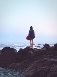 Rear view of woman standing on rock at beach against sky