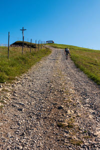 Rear view of man walking on dirt road against clear blue sky