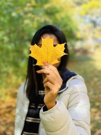 Portrait of woman holding maple leaf during autumn