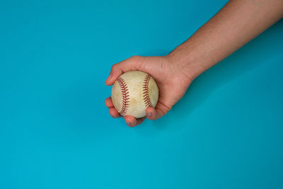 Close-up of hand holding a ball against blue background