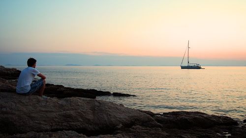 Man looking at sea while relaxing on rock during sunset