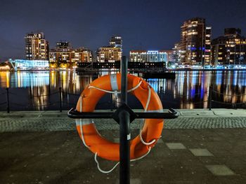 Illuminated lamp post by river against buildings at night