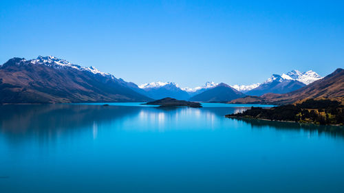 Scenic view of lake and mountains against clear blue sky