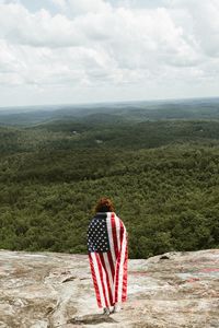Rear view of woman holding american flag while standing on mountain