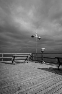 Empty benches and telescope on floorboard by baltic sea against cloudy sky