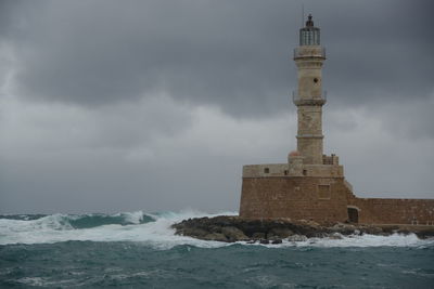 Lighthouse on building by sea against sky