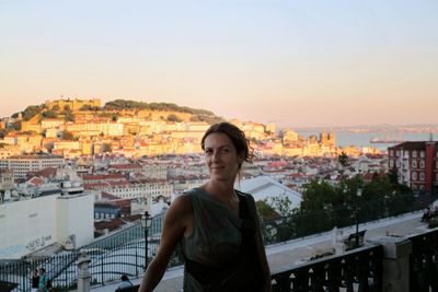 Portrait of woman standing against cityscape in balcony during sunset