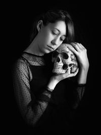 Sad woman holding human skull while standing against black background