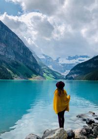 Rear view of woman looking at lake while standing on rock against cloudy sky