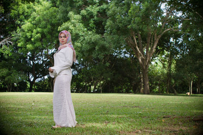 Portrait of woman wearing scarf while standing on field by trees