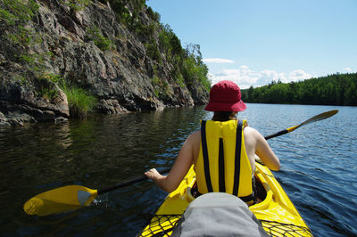 Rear view of woman kayaking on sea against blue sky