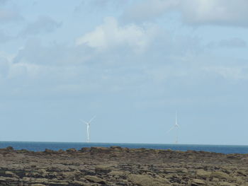 Wind turbines on land by sea against sky