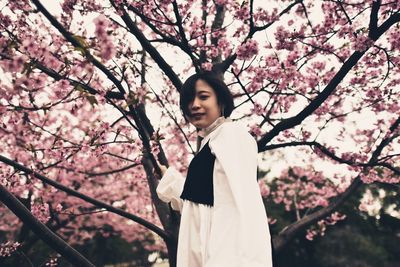 Low angle view of woman standing by cherry blossom tree