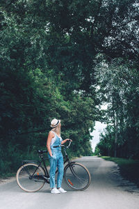 Side view of teenage girl with bicycle standing on road