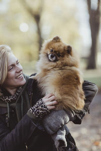 Smiling woman playing while embracing fluffy pomeranian dog at park