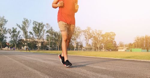 Low section of man running on road against clear sky during sunset