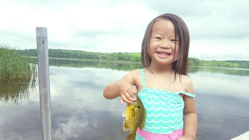 Happy girl standing by lake against sky