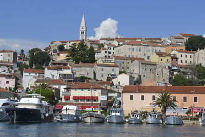 Sailboats in city by sea against sky