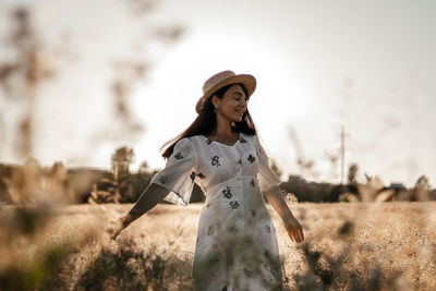 A girl in a wheat field wearing a dress and a straw hat. the girl is circling in the field.