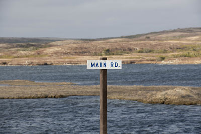 Information sign by sea against sky