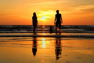 Silhouette men on beach against sky during sunset