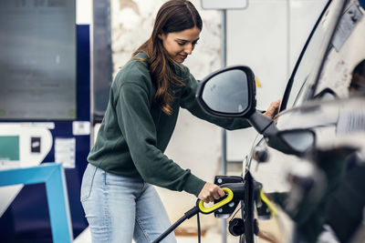 Smiling woman plugging charger in car at electric vehicle charging station