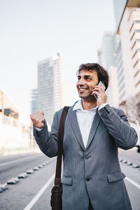 Smiling businessman talking over mobile phone while standing on road