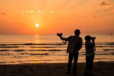 People photographing at beach against sky during sunset