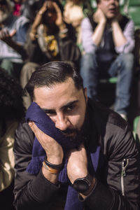 Sad male supporter sitting with scarf after defeat in game at stadium