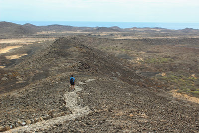 Rear view of man walking on mountain against sky