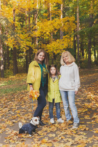 Full length portrait of friends standing on tree during autumn